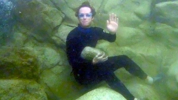 Holding a rock underwater, sitting at the bottom of a rockpool